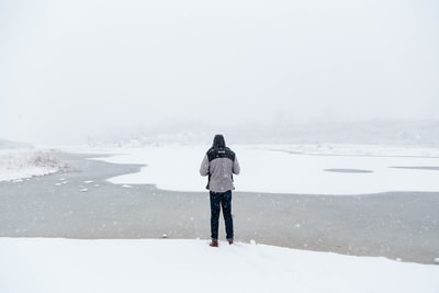 男人站在雪领域面临河
